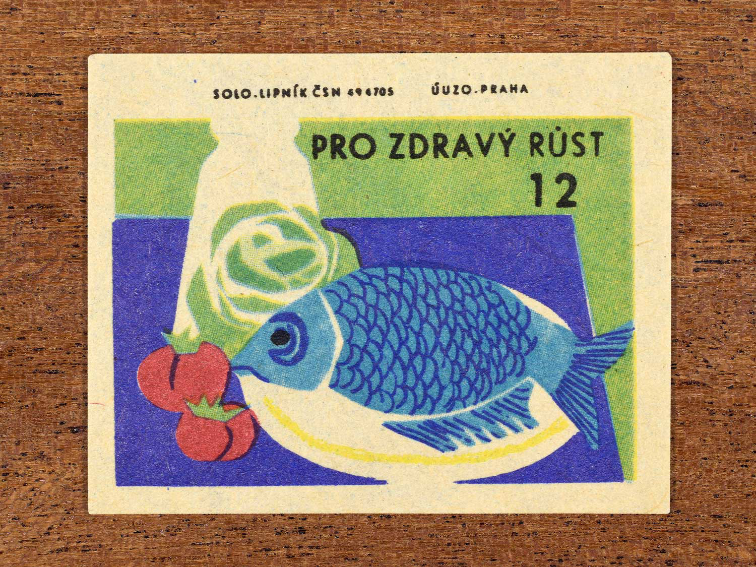 Vintage c. 1965 Czech matchbox label showing a large fish on a plate and vegetables arranged on a table. Produced by Solo Lipník match factory to promote the health benefits proper nutrition, daily meal routines, and everyday household habits.