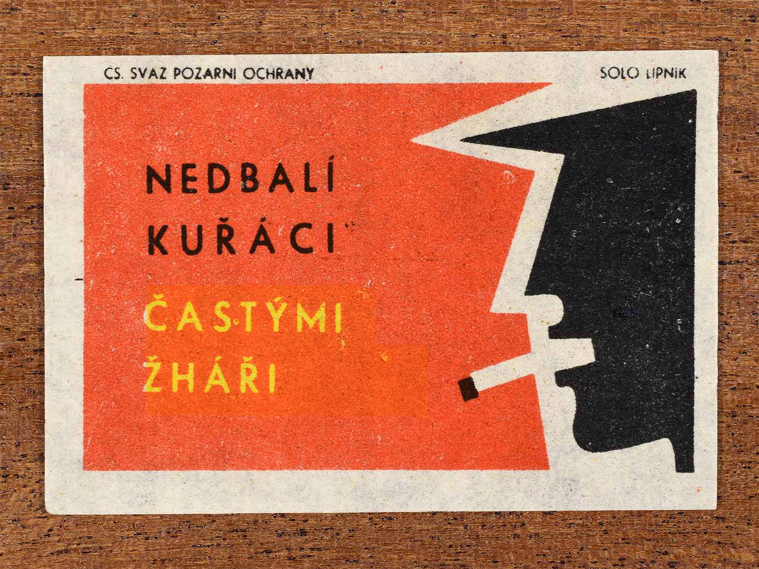 Vintage 1963 Czech matchbox label showing a side profile of a face with a cigarette in its mouth. In red, black and white colours. Produced by the Solo Lipník match factory to warn against careless smoking.