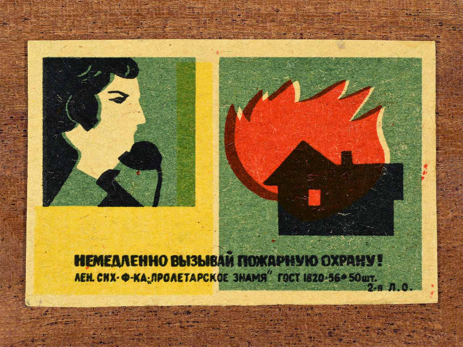 Vintage 1962 Soviet matchbox label showing a person calling emergency services during a house fire. In yellow, green, red and black colours. Produced by the Proletarian Banner match factory to promote immediate reporting of fires.