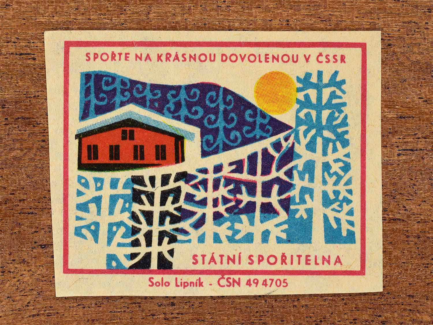 Vintage 1968 Czech matchbox label showing a winter cabin surrounded by snow-covered trees. Produced by the Solo Lipník match factory to promote saving money for holidays in the Czechoslovak Socialist Republic.