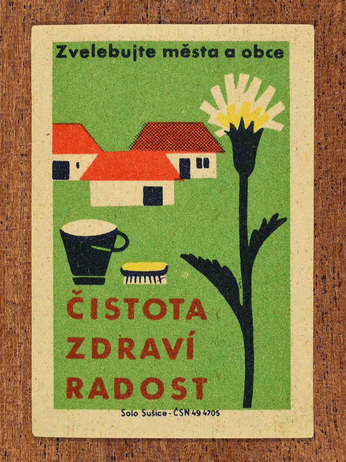 Vintage 1961 Czech matchbox label showing a bucket, brush, and soap alongside a large blooming wildflower in front of village houses, on a green background. Produced by the Solo Sušice match factory to promote household hygiene, health, and civic pride.