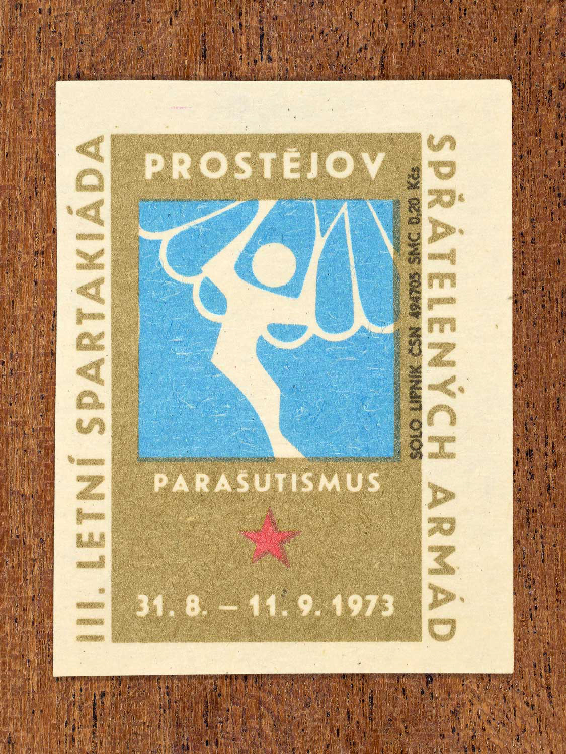 Vintage 1973 Czech matchbox label showing a simplified white parachutist with open chute on a blue and gold background. Produced by the Solo Lipník match factory to promote physical training and demonstrate collective military readiness among allied armies.