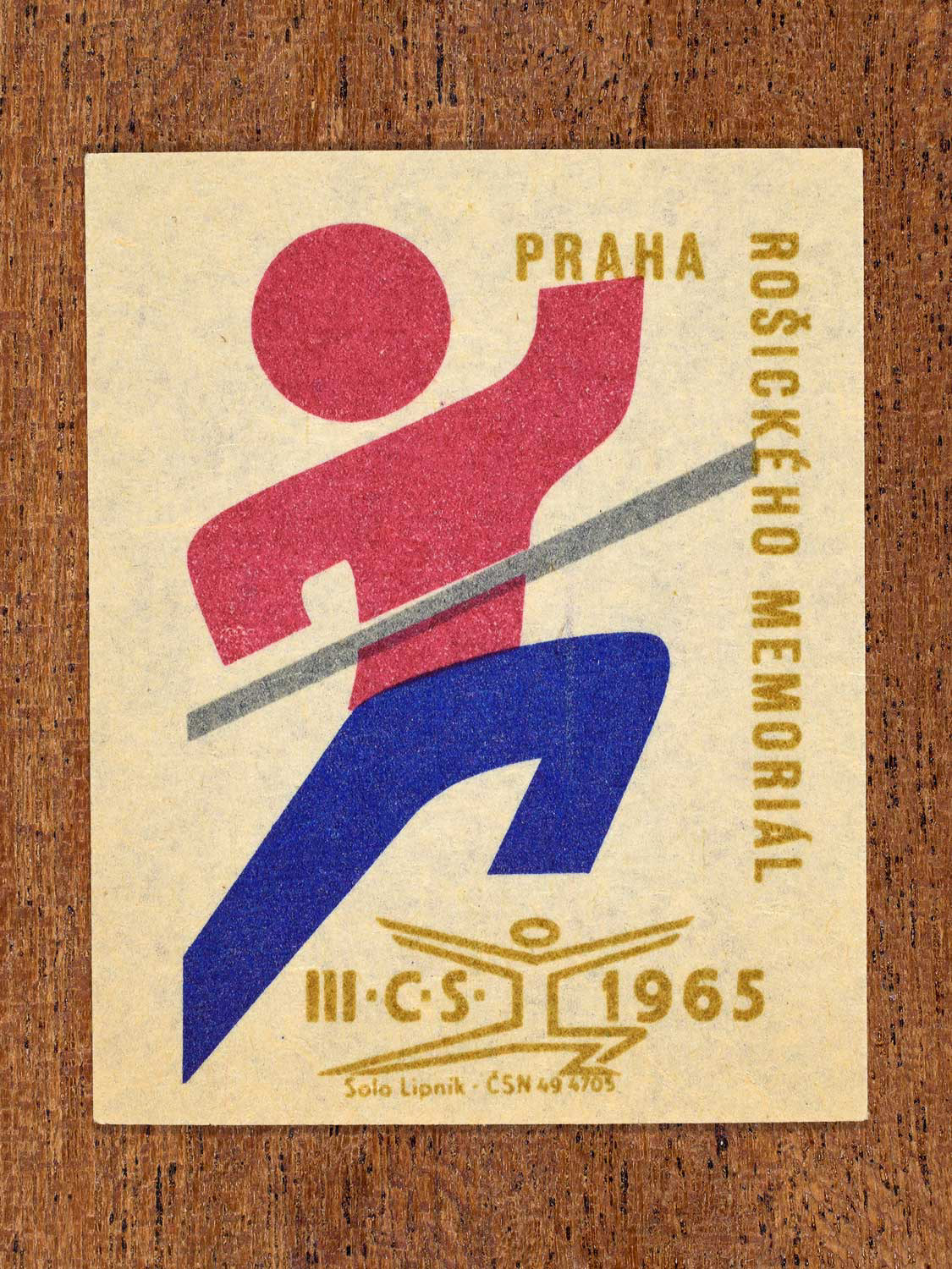 Vintage 1965 Czechoslovak matchbox label showing a stylised figure crossing a finish line. In blue, red and gold colours. Produced by the Solo Lipník match factory as a memorial to an athlete.