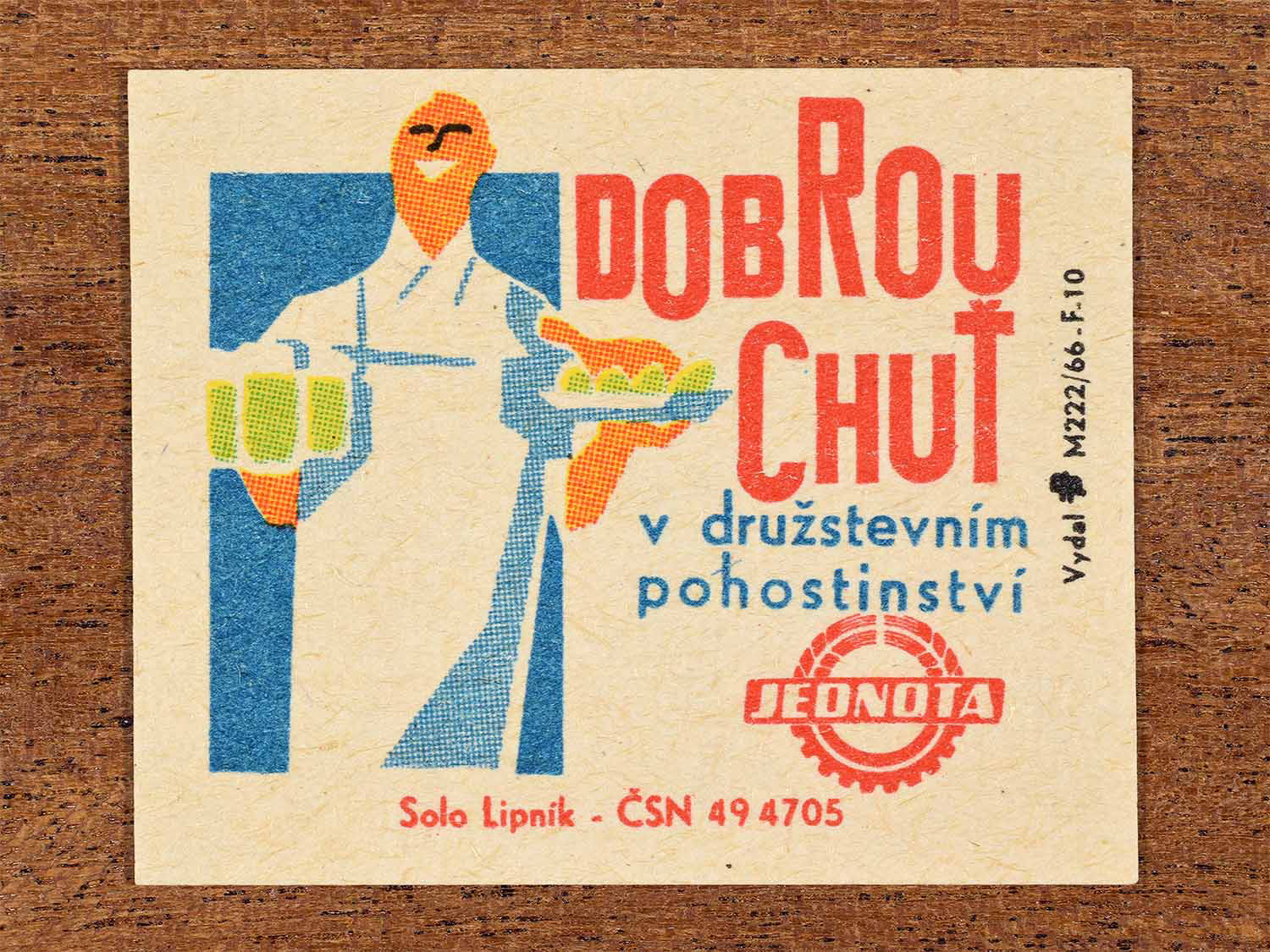 Vintage c. 1966 Czech matchbox label showing a smiling waiter carrying drinks and food trays in bold geometric colours. Produced by the Solo Lipník match factory to promote dining in Jednota cooperative restaurants.