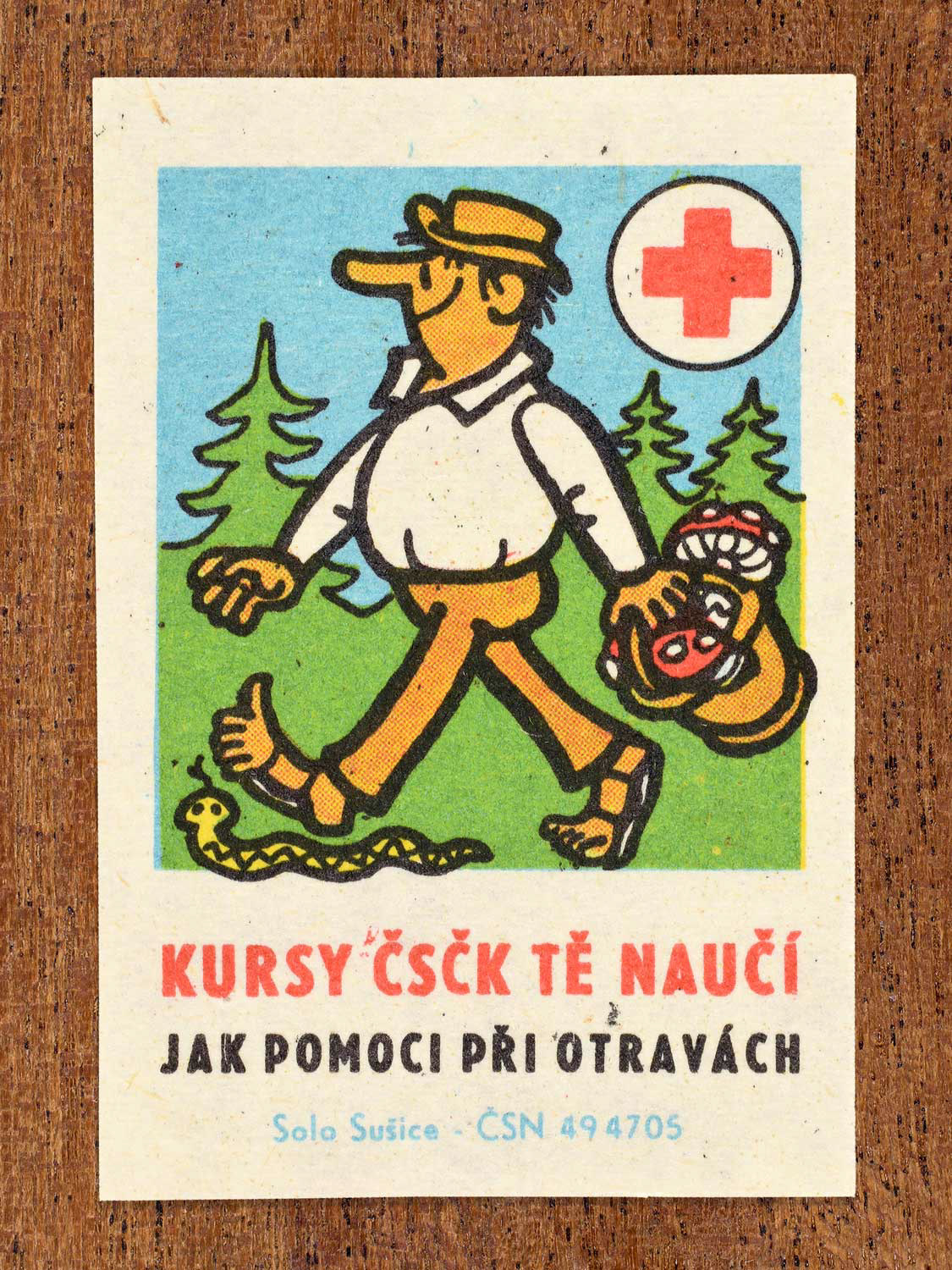 Vintage c. 1966 Czech matchbox label showing a man walking in nature while carrying a basket of wild mushrooms, and about to step on a snake. Produced by the Solo Sušice match factory to promote first-aid education and emergency response to poisoning in cooperation with the Czechoslovak Red Cross.