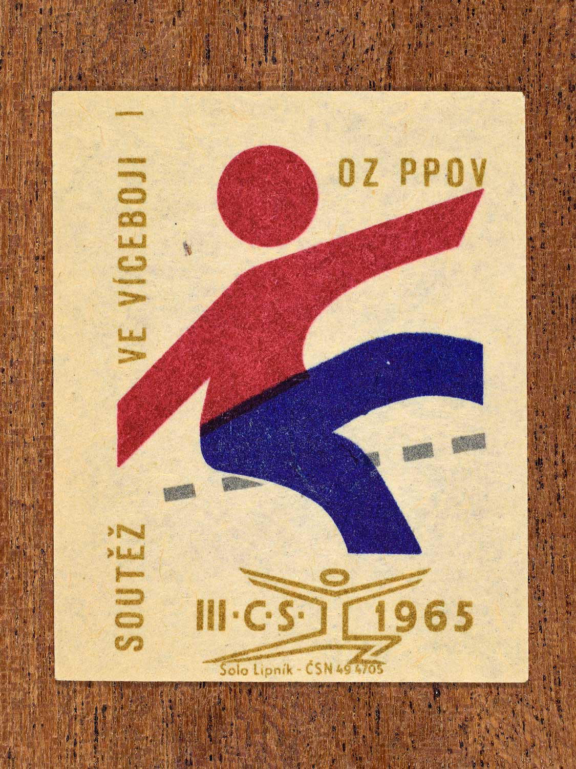 Vintage 1965 Czechoslovak matchbox label showing an abstract athlete figure, in blue, red and gold colours. Produced by the Solo Lipník match factory to promote physical fitness and sporting achievement.