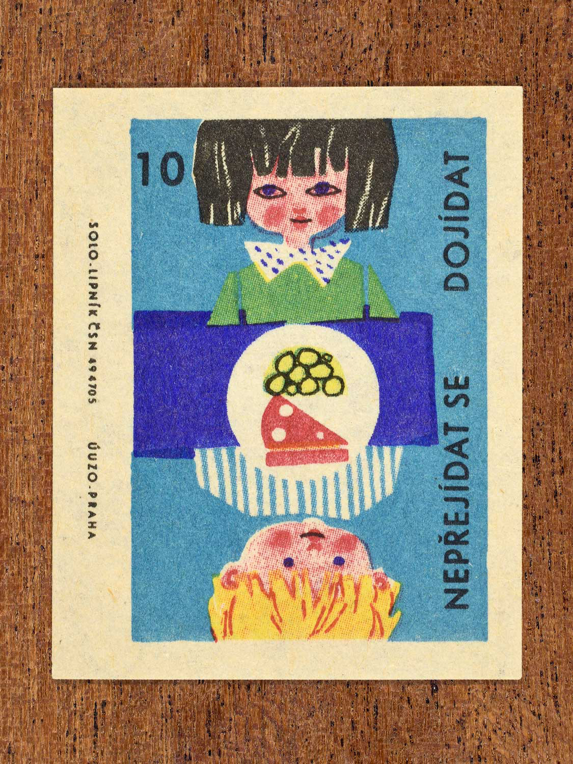 Vintage c. 1965 Czech matchbox label showing two children eat at a table and a large plate of food in-between them. Produced by Solo Lipník match factory to promote the health benefits proper nutrition, daily meal routines, and everyday household habits.