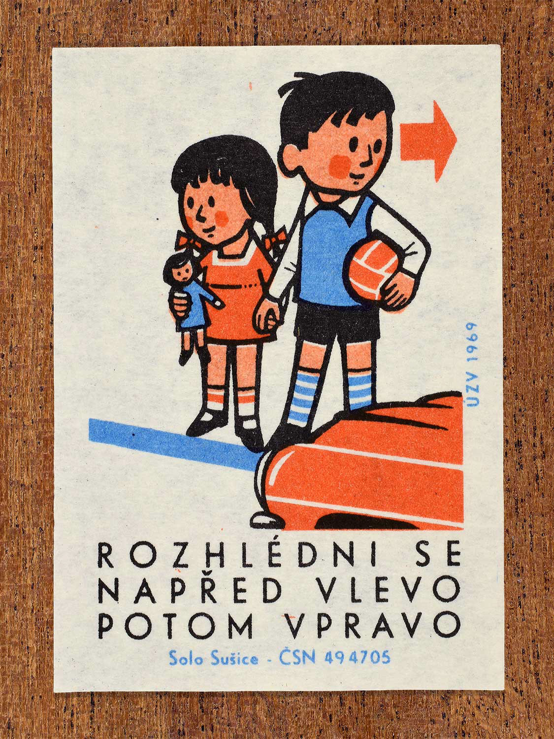 Vintage 1969 Czech matchbox label showing a young boy and girl holding hands, with the boy holding a ball, preparing to cross a road near a red car. Produced by the Solo Sušice match factory to promote safe road crossing habits among children."