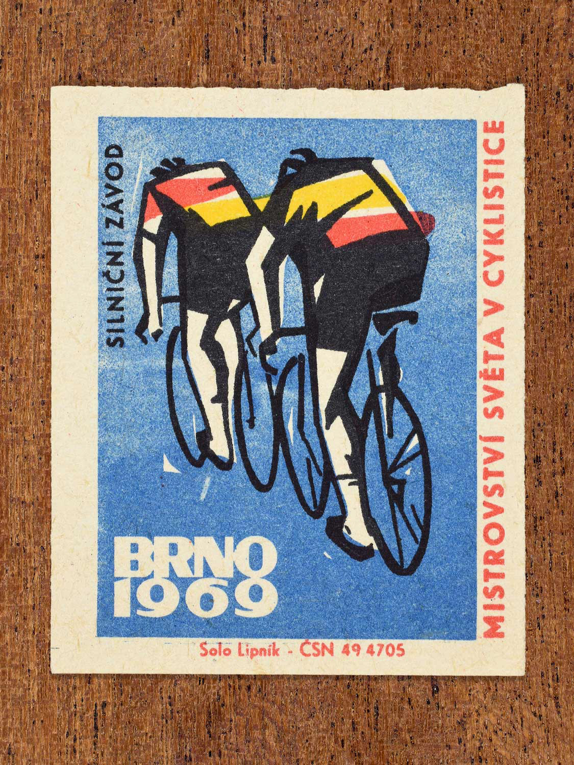 Vintage 1969 Czech matchbox label showing two stylised road cyclists riding in formation, on a blue background. Produced by the Solo Lipník match factory to promote the road race event of the cycling championship in Brno, Czechoslovakia.