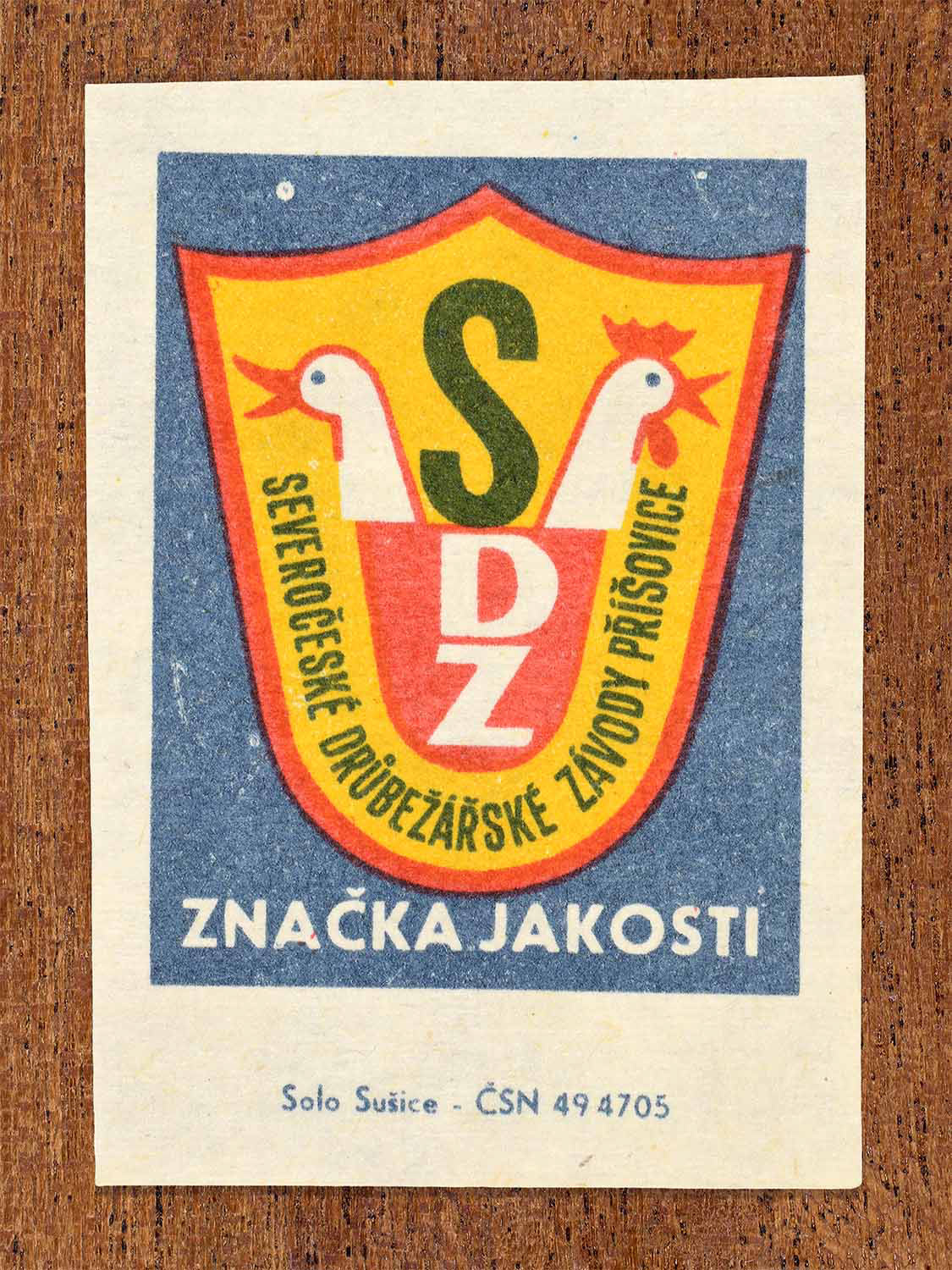 Vintage c. 1966 Czech matchbox label showing a shield-shaped quality mark for the North Bohemian Poultry Works with stylised chickens and bold lettering. Produced by the Solo Lipník match factory to certify quality poultry production.