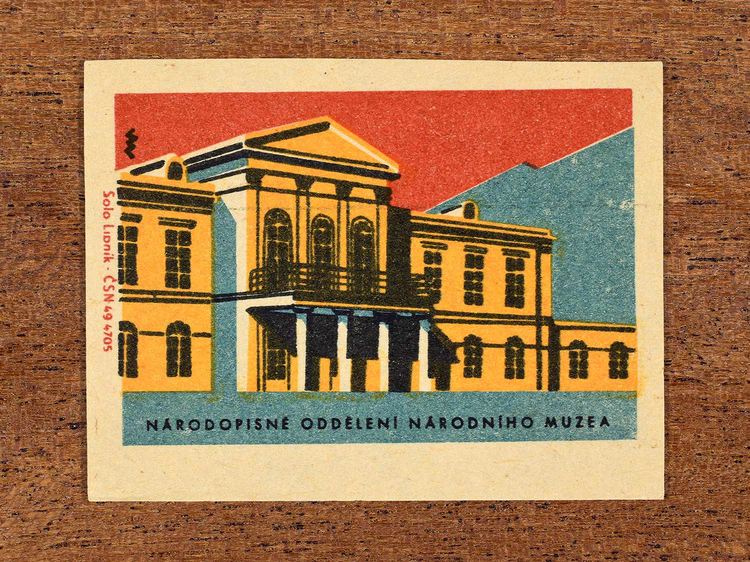 Vintage 1964 Czechoslovakia matchbox label showing the Národopisné Oddělení Národního Muzea (Ethnographic Department of the National Museum) in yellow, red and teal colours. Produced by the Solo Lipník match factory to promote domestic historical heritage and municipal institutions across the state.