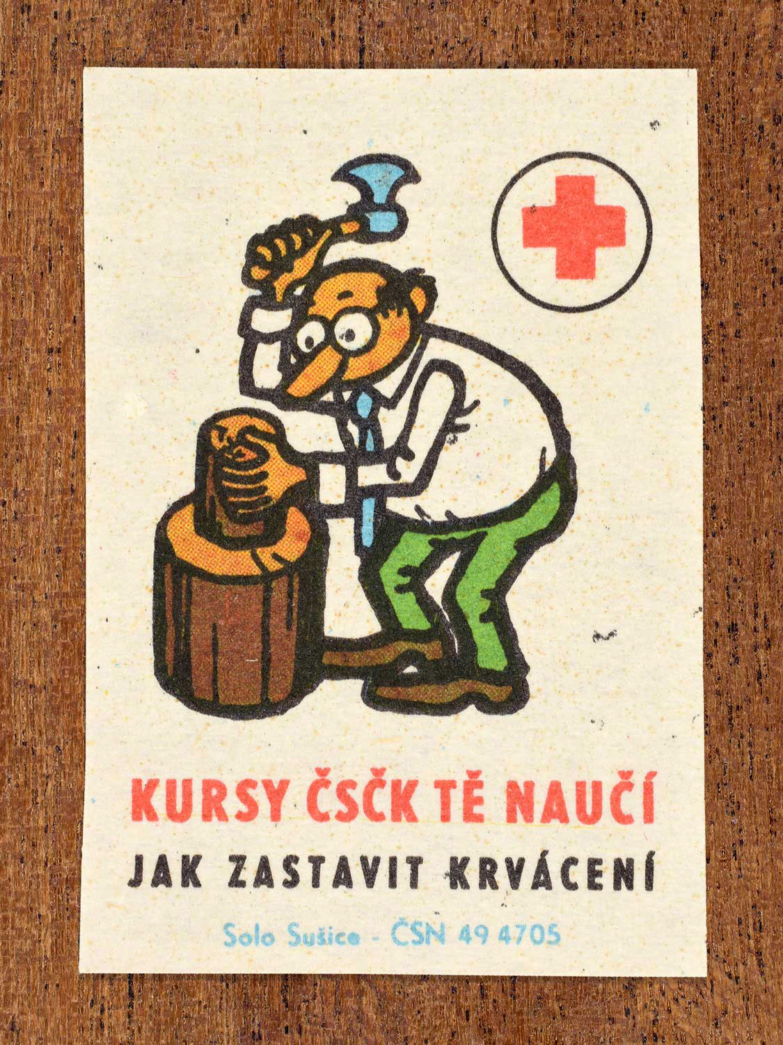 Vintage c. 1966 Czech matchbox label showing a man chopping wood and about to injure himself. Produced by the Solo Sušice match factory to promote first-aid education in cooperation with the Czechoslovak Red Cross.