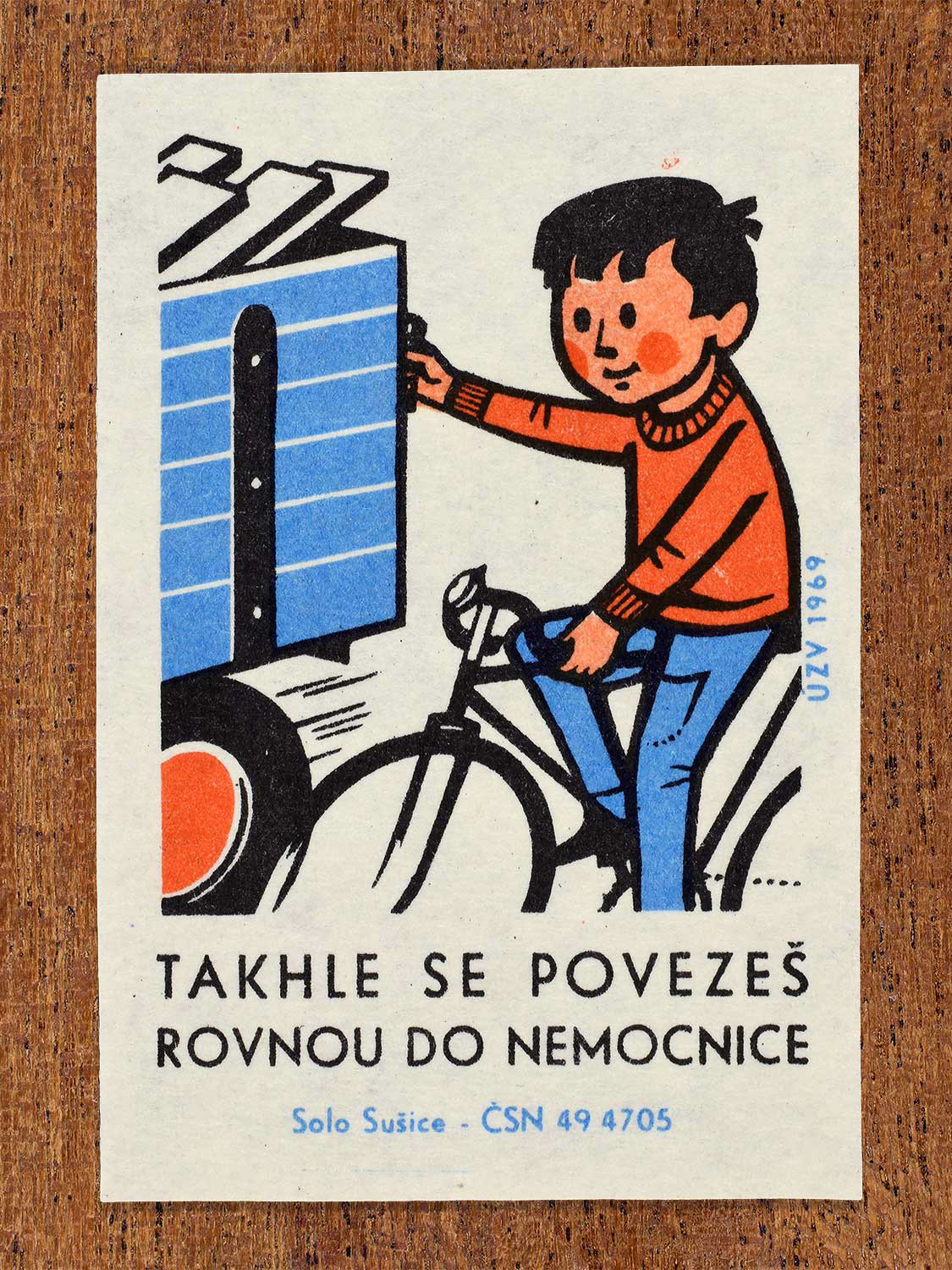 Vintage 1969 Czech matchbox label showing a reckless boy holding onto the back of a moving blue flatbed truck while riding his bicycle. Produced by the Solo Sušice match factory to promote bicycle safety and warn against hitching rides on motor vehicles.