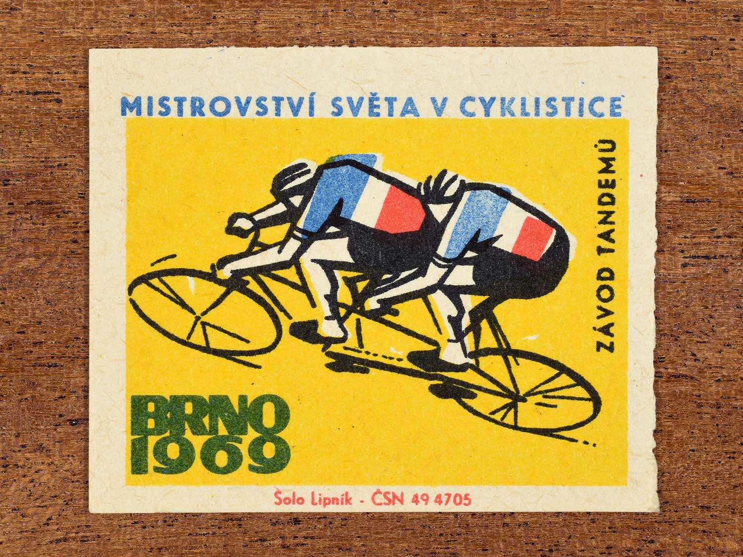 Vintage 1969 Czech matchbox label showing stylised tandem cycling race in motion, on a yellow background. Produced by the Solo Lipník match factory to promote tandem cycling events at a championship in Brno, Czechoslovakia.