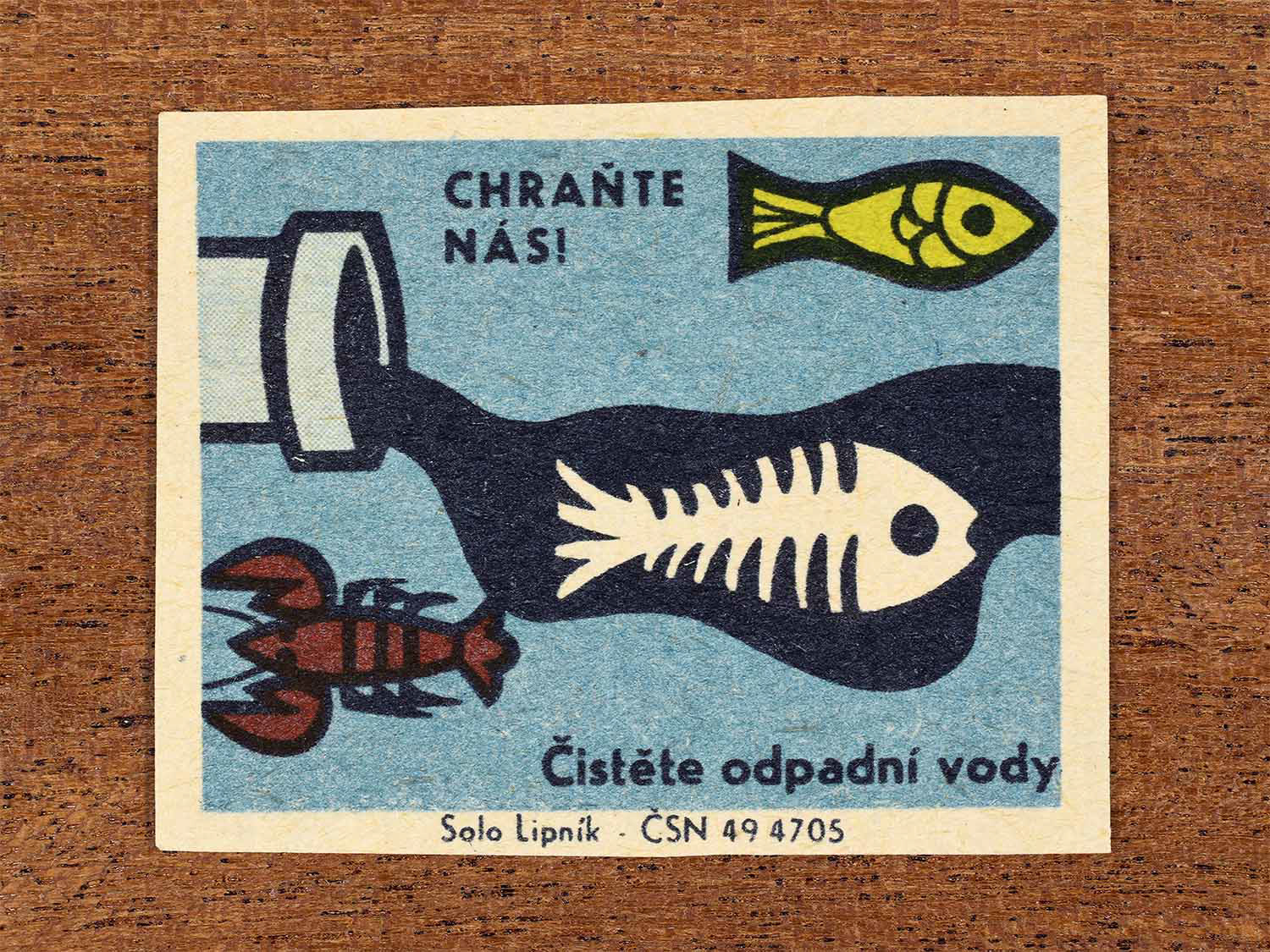 Vintage 1966 Czech matchbox label showing a fish skeleton in wastewater from a drainage pipe. In blue, green and red colours. Produced by the Solo Lipník match factory to promote cleaning wastewater to protect aquatic life.