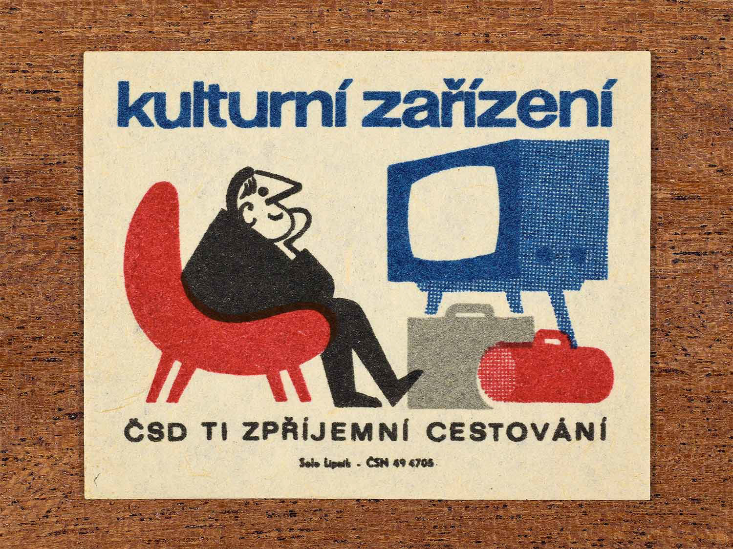 Vintage c. 1964 Czech matchbox label showing a passenger enjoying television onboard a train, illustrated in blue, red and black. Produced by the Solo Lipník match factory to promote onboard cultural amenities provided by ČSD.