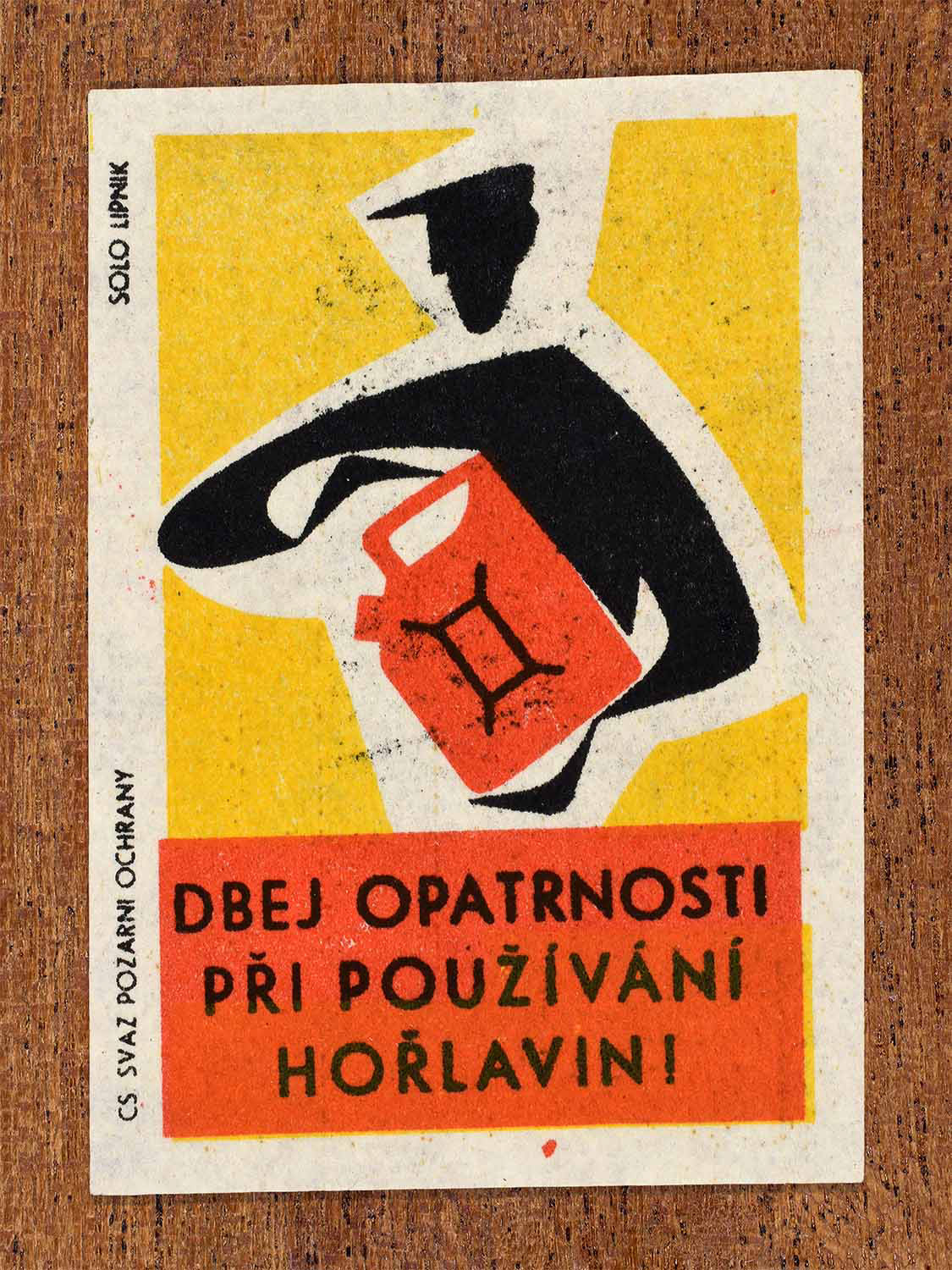 Vintage 1963 Czech matchbox label showing a person holding a fuel can in red, yellow and black colours. Produced by the Solo Lipník match factory to warn about careful handling of flammable materials.