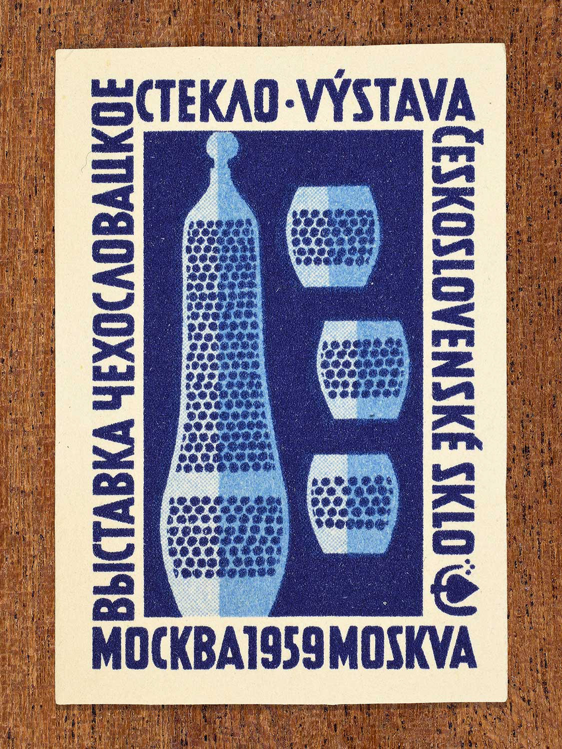 Phillumeny graphic featuring several abstract glass vessels in blue colours depicted on a Czechoslovak matchbox label. The design functions to showcase Czechoslovak glass craftsmanship as exhibited at an event in Moscow, 1959.