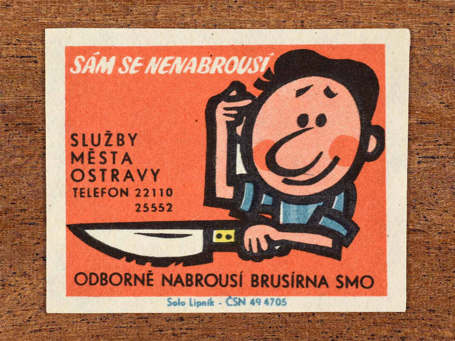 Vintage 1967 Czech matchbox label showing a cartoon man presenting a knife for sharpening. Produced by the Solo Lipník match factory to promote municipal professional sharpening services.