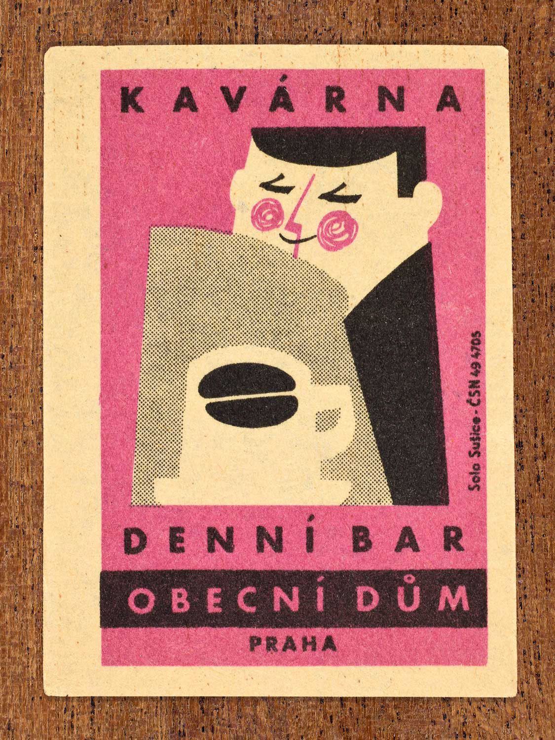 Vintage 1964 Czech matchbox label showing a stylised person with a coffee mug reading a newspaper, on pink background. Produced by the Solo Sušice match factory to promote a café inside Prague's Obecní dům (Municipal House) in Czechoslovakia.