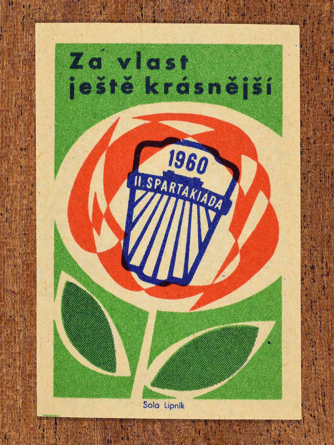 Vintage 1960 Czech matchbox label showing the emblem of the 1960 Second Spartakiad inside a stylised flower design in red, green and blue colours. Produced by the Solo Lipník match factory to celebrate socialist mass sporting events and national unity.