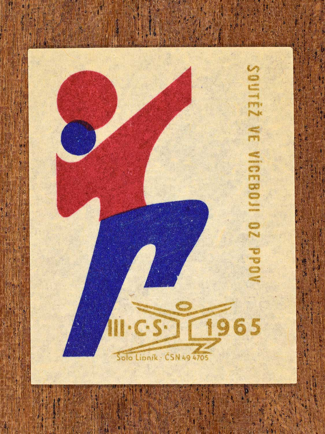Vintage 1965 Czechoslovak matchbox label showing an abstract athlete figure, in blue, red and gold colours. Produced by the Solo Lipník match factory to promote physical fitness and sporting achievement.