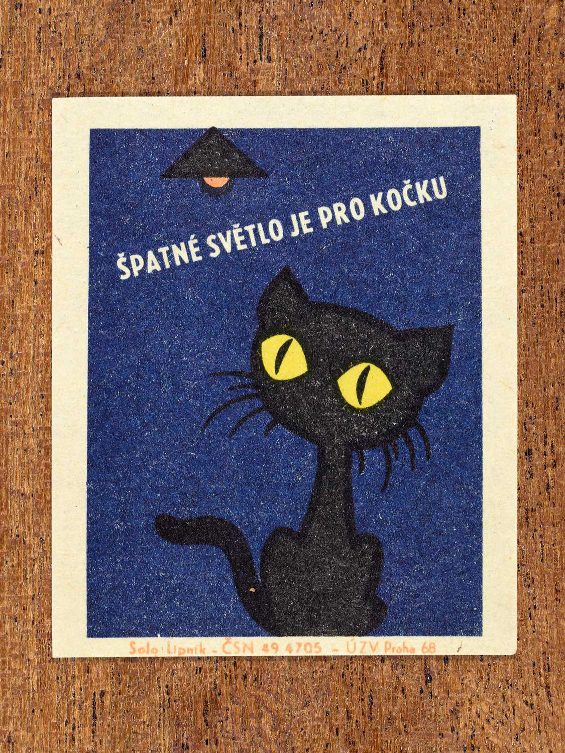 Vintage 1968 Czech matchbox label featuring a cartoon black cat with yellow eyes looking up to a hanging light, on blue background. Produced by Solo Lipník match factory to promote proper lighting and maintenance for eye health and safe work practices.