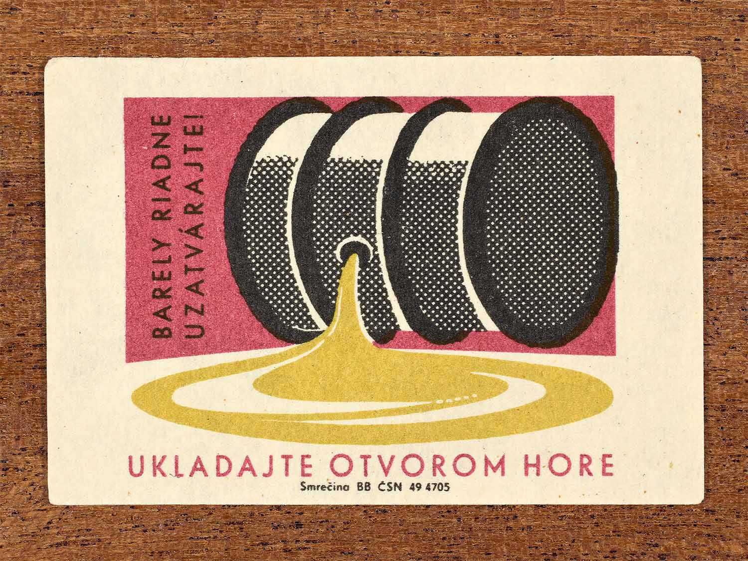 Vintage 1960s Czechoslovak matchbox label showing a metal barrel lying on its side with liquid spilling onto the floor, in black, red and yellow. Produced by the Smrečina match factory to warn that barrels must be properly sealed and stored with the opening facing up.
