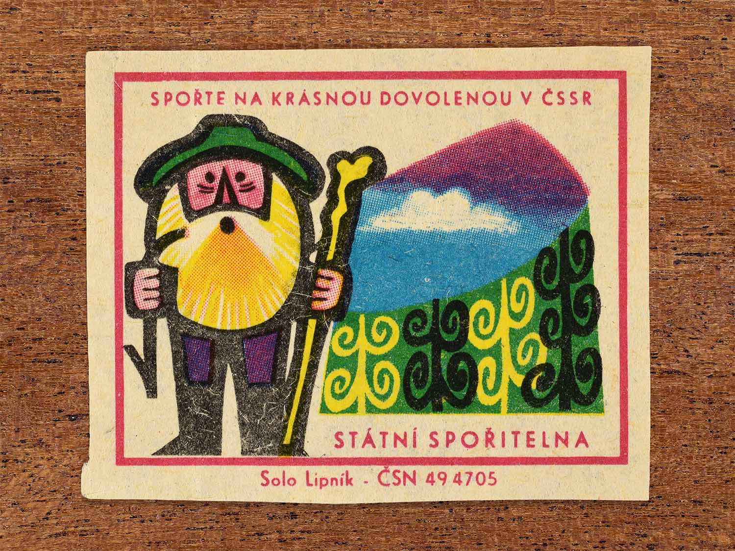 Vintage 1968 Czech matchbox label showing a stylised mountain hiker with walking stick and alpine landscape. Produced by the Solo Lipník match factory to promote saving money for holidays in the Czechoslovak Socialist Republic.