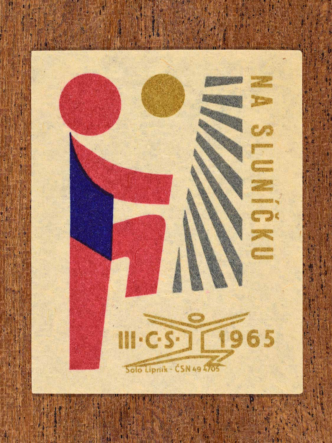 Vintage 1965 Czechoslovak matchbox label showing an abstract illustration of a sporting figure, sun and rays. In blue, red and gold colours. Produced by the Solo Lipník match factory to promote physical fitness and sporting achievement.