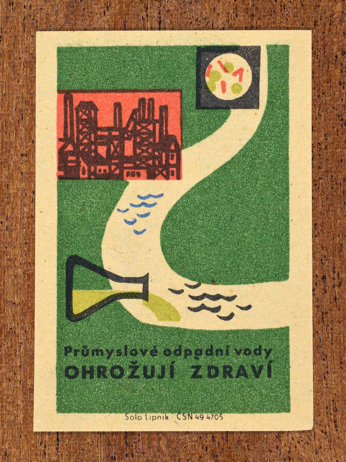 Vintage c. 1963 Czech matchbox label showing a factory releasing industrial wastewater into a river, in green, red and black colours. Produced by Solo Lipník match factory warning that such waste threatens human health.