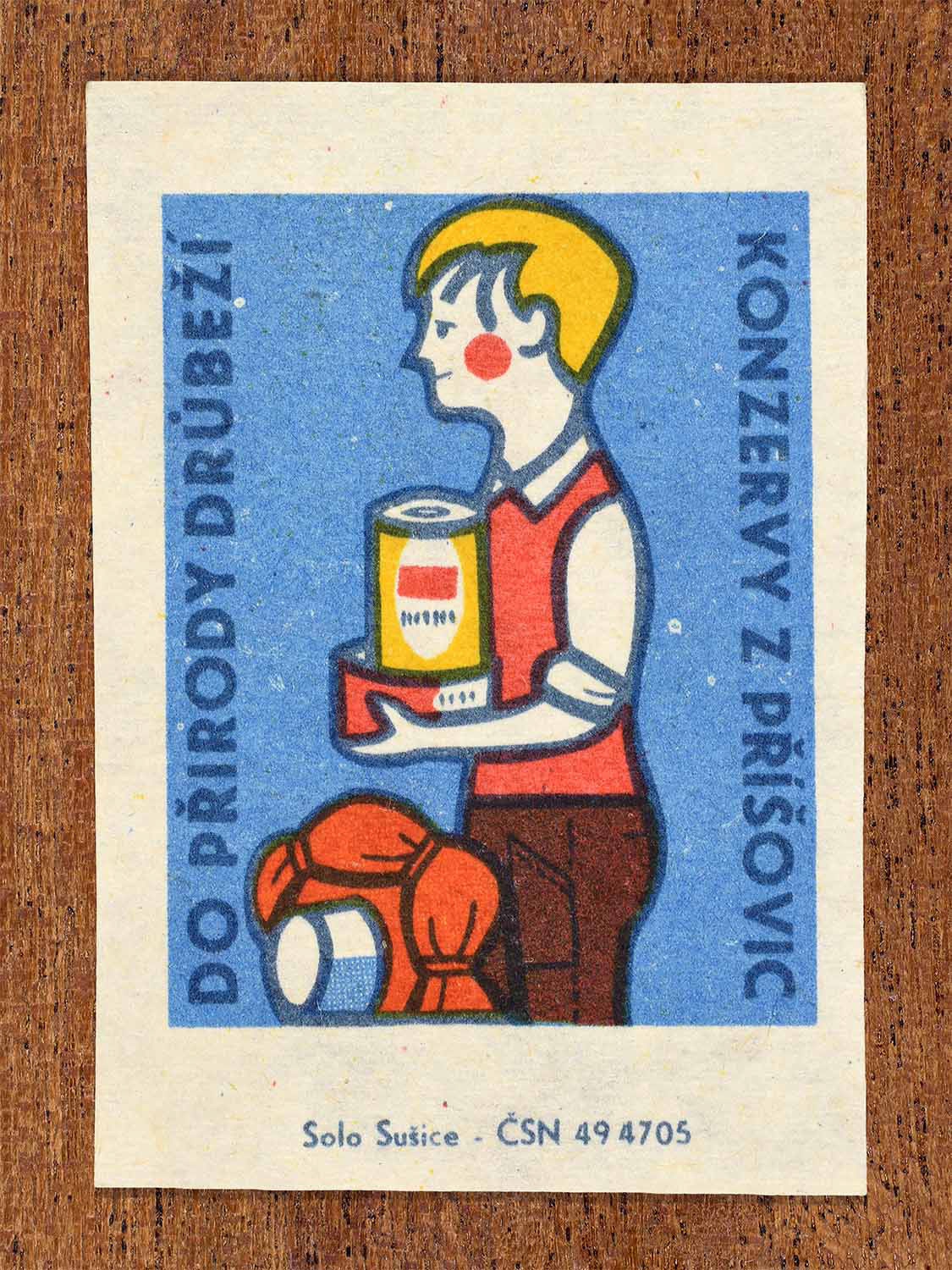Vintage c. 1966 Czech matchbox label showing a man carrying canned poultry food for outdoor use in bold blue, red and yellow colours. Produced by the Solo Lipník match factory to promote preserved poultry as practical outdoor food.