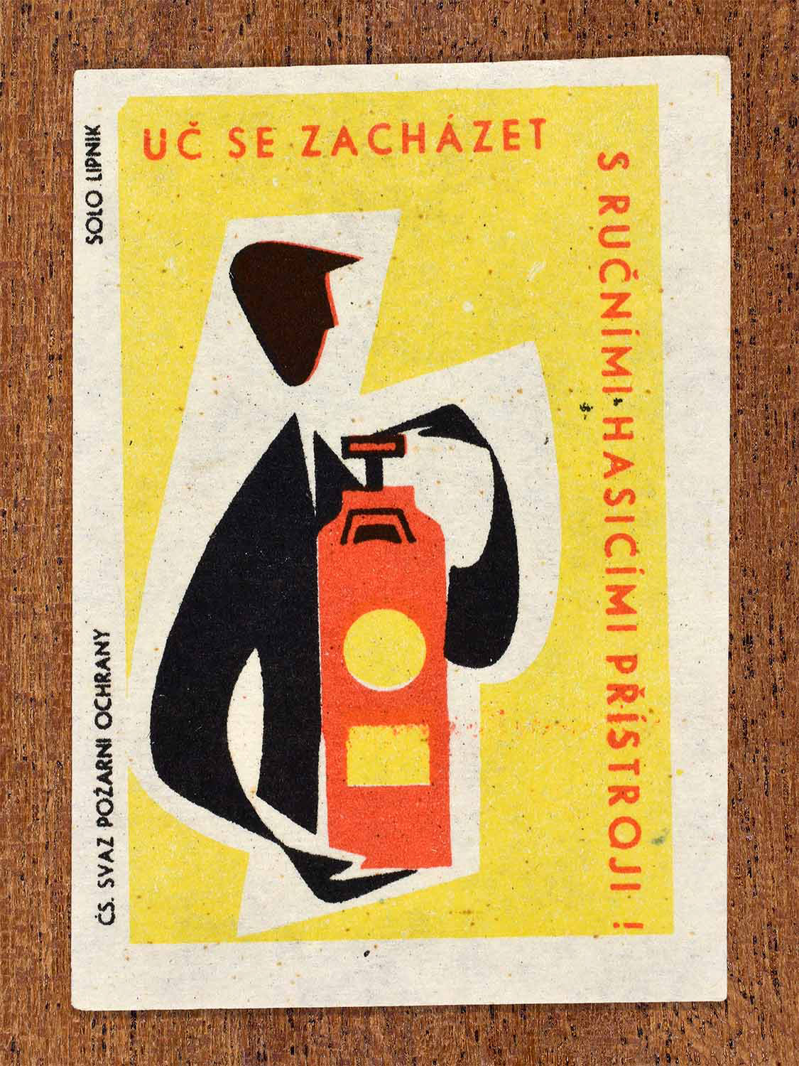 Vintage 1963 Czech matchbox label showing a person using a fire extinguisher in red, yellow and black colours. Produced by the Solo Lipník match factory to promote fire extinguisher training.