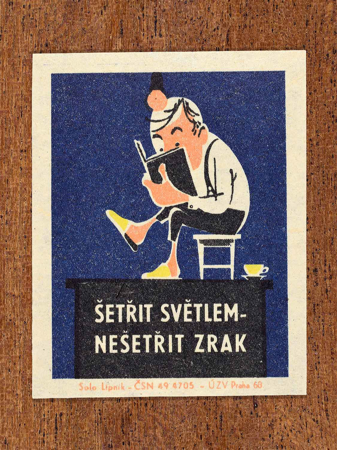 Vintage 1968 Czech matchbox label featuring a cartoon person sitting on a chair looking closely at a book with a hanging bulb above, on blue background. Produced by Solo Lipník match factory to promote proper lighting and maintenance for eye health and safe work practices.