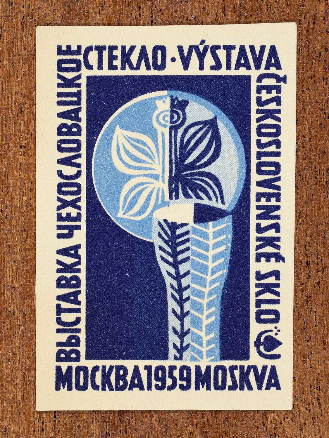 An abstract phillumeny graphic featuring abstract glass ornaments in blue colours depicted on a Czechoslovak matchbox label by an unknown factory. The design functions to showcase Czechoslovak glass craftsmanship as exhibited at an event in Moscow, 1959.