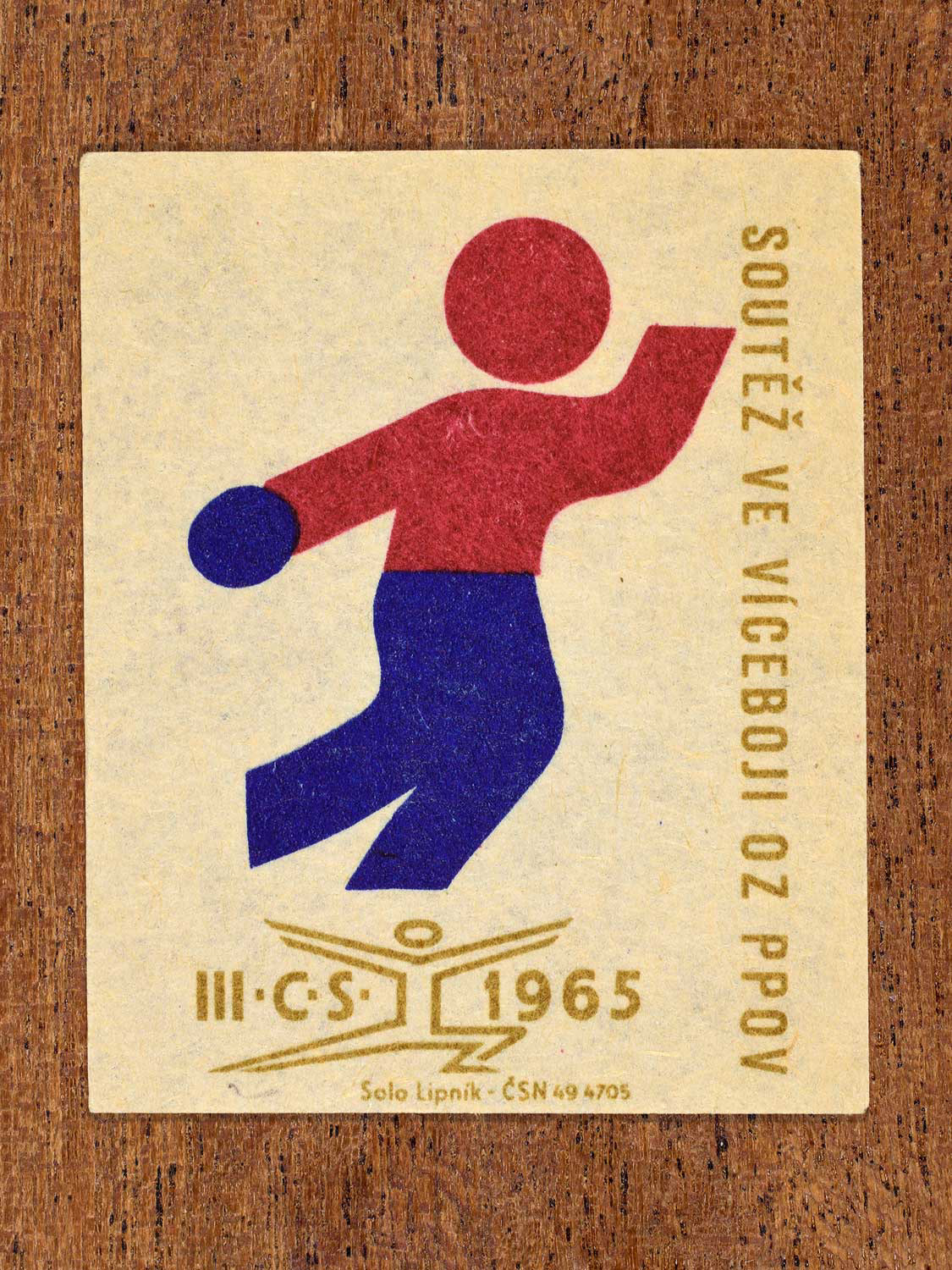 Vintage 1965 Czechoslovak matchbox label showing an abstract athlete figure, in blue, red and gold colours. Produced by the Solo Lipník match factory to promote physical fitness and sporting achievement.