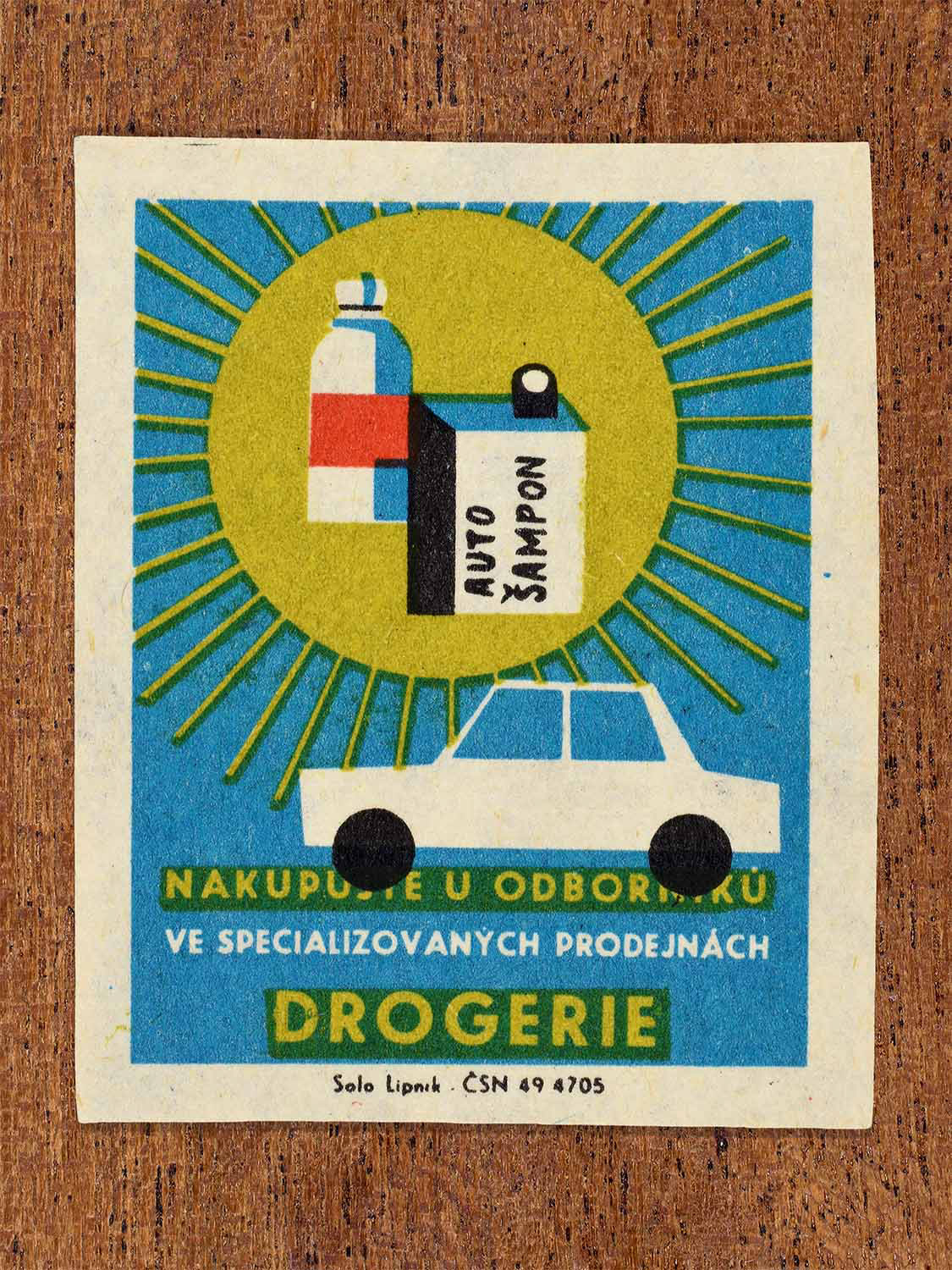 Vintage c. 1967 Czech matchbox label showing car shampoo and cleaning products beside a car in blue, yellow, red and black colours. Produced by the Solo Lipník match factory to promote shopping for toiletries and household goods in specialised retail stores.