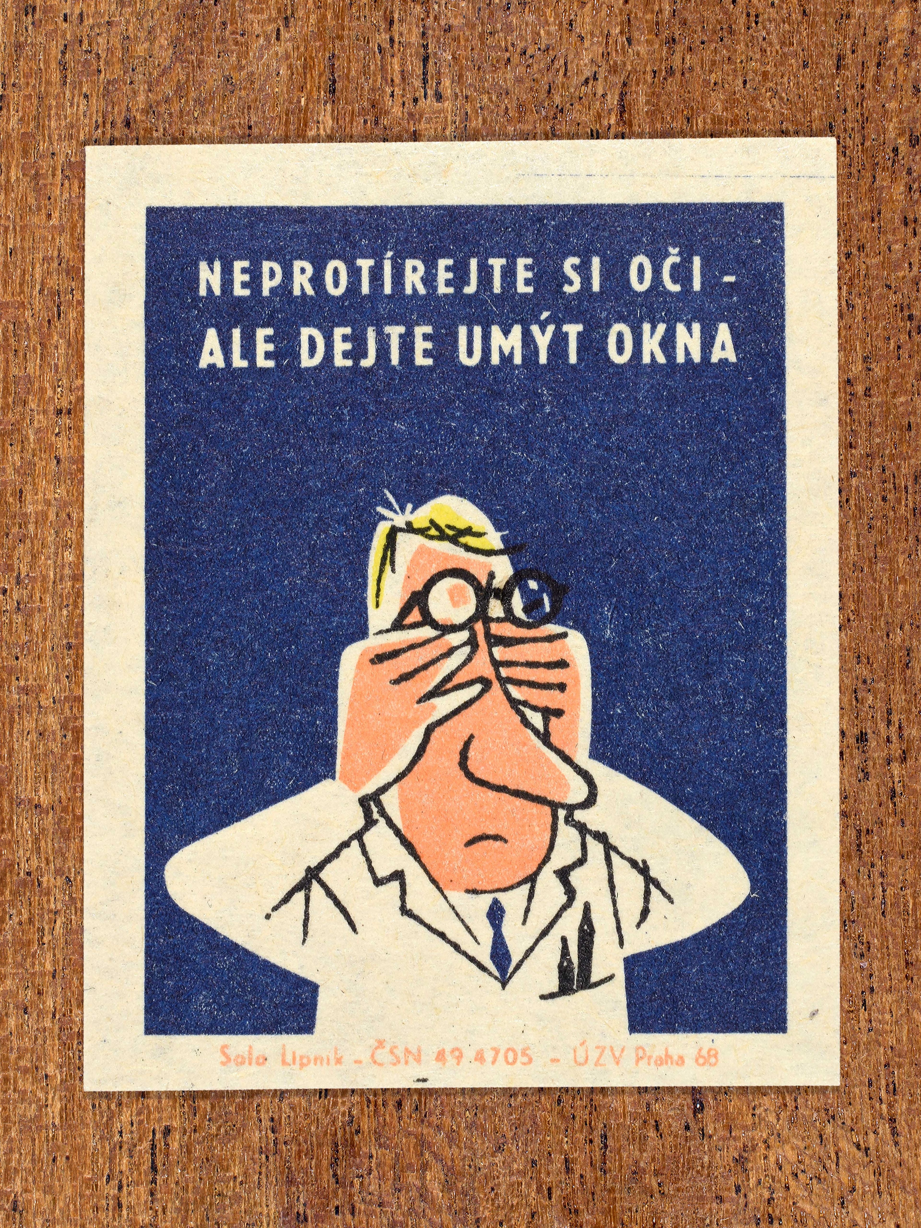 Vintage 1968 Czech matchbox label featuring a cartoon person wearing a lab coat and glasses rubbing their eyes, on blue background. Produced by Solo Lipník match factory to promote proper lighting and maintenance for eye health and safe work practices.