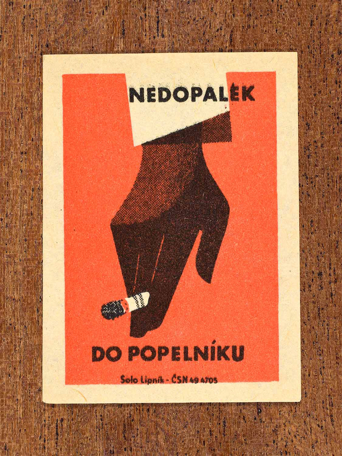 Vintage 1964 Czech matchbox label showing a hand holding a cigarette butt in red and black colours. Produced by the Solo Lipník match factory to promote fire prevention and responsible smoking behaviour.