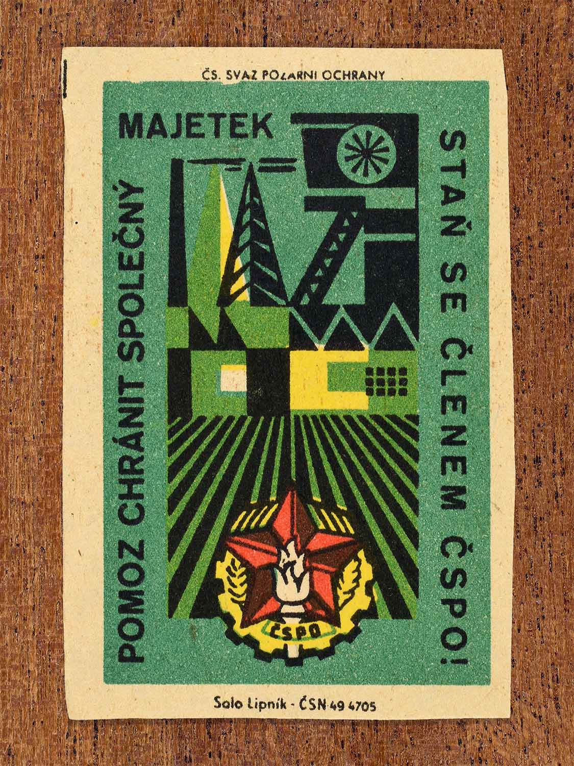 Vintage c. 1961 Czech matchbox label showing an industrial landscape with fields, buildings, and a red star emblem. In green, red, yellow and black colours. Produced by the Solo Lipník match factory to encourage joining the fire protection union to help protect shared property.