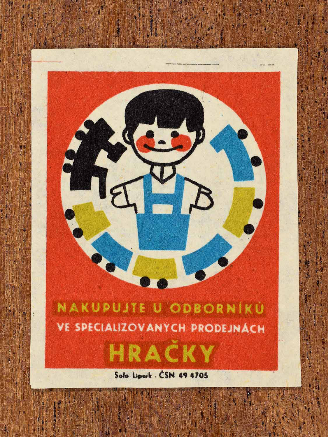 Vintage c. 1967 Czech matchbox label showing a smiling child surrounded by a toy train. In red, blue, yellow and black colours. Produced by the Solo Lipník match factory to promote shopping for toys in specialised retail stores.