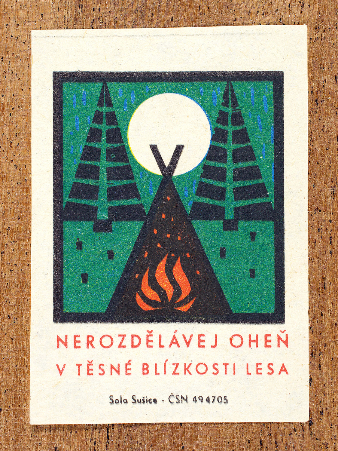 1968 Czechoslovak matchbox label by Solo Sušice showing a campfire under trees and a moon. Used as a public service message warning campers to keep flames far from woodland. Label 7 of 10 in the Fire Hazards Series.