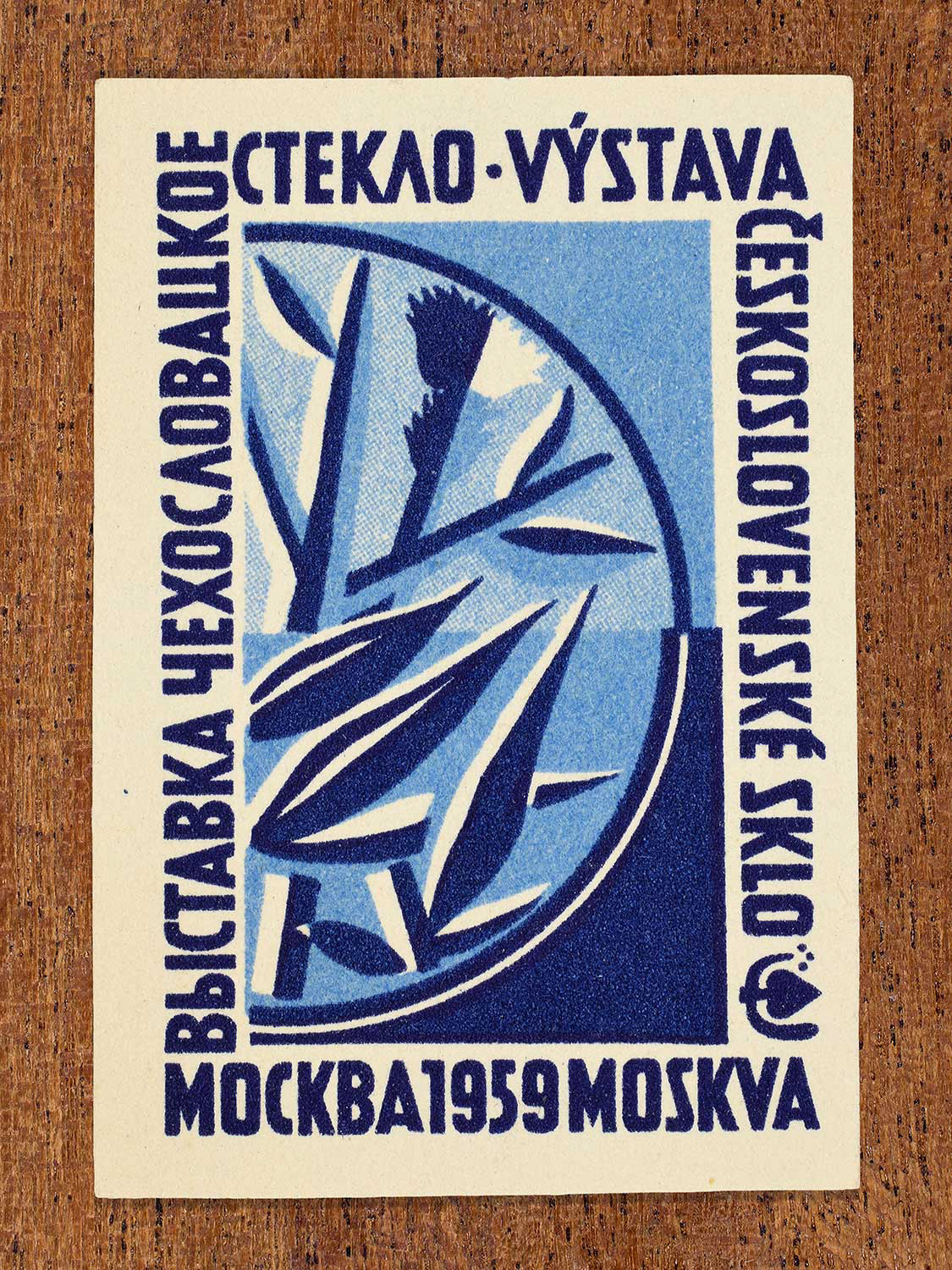 An illustration of a stylised glass design on a blue backdrop depicted on a matchbox label. The design functions to celebrate the artistry of Czechoslovak glass craftsmanship as exhibited at an event in Moscow, 1959.
