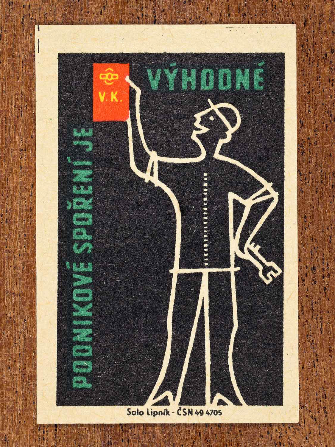 Vintage 1960 Czech matchbox label showing a stylised worker raising a saving book, on black background. Produced by the Solo Lipník match factory to promote advantageous workplace savings schemes.
