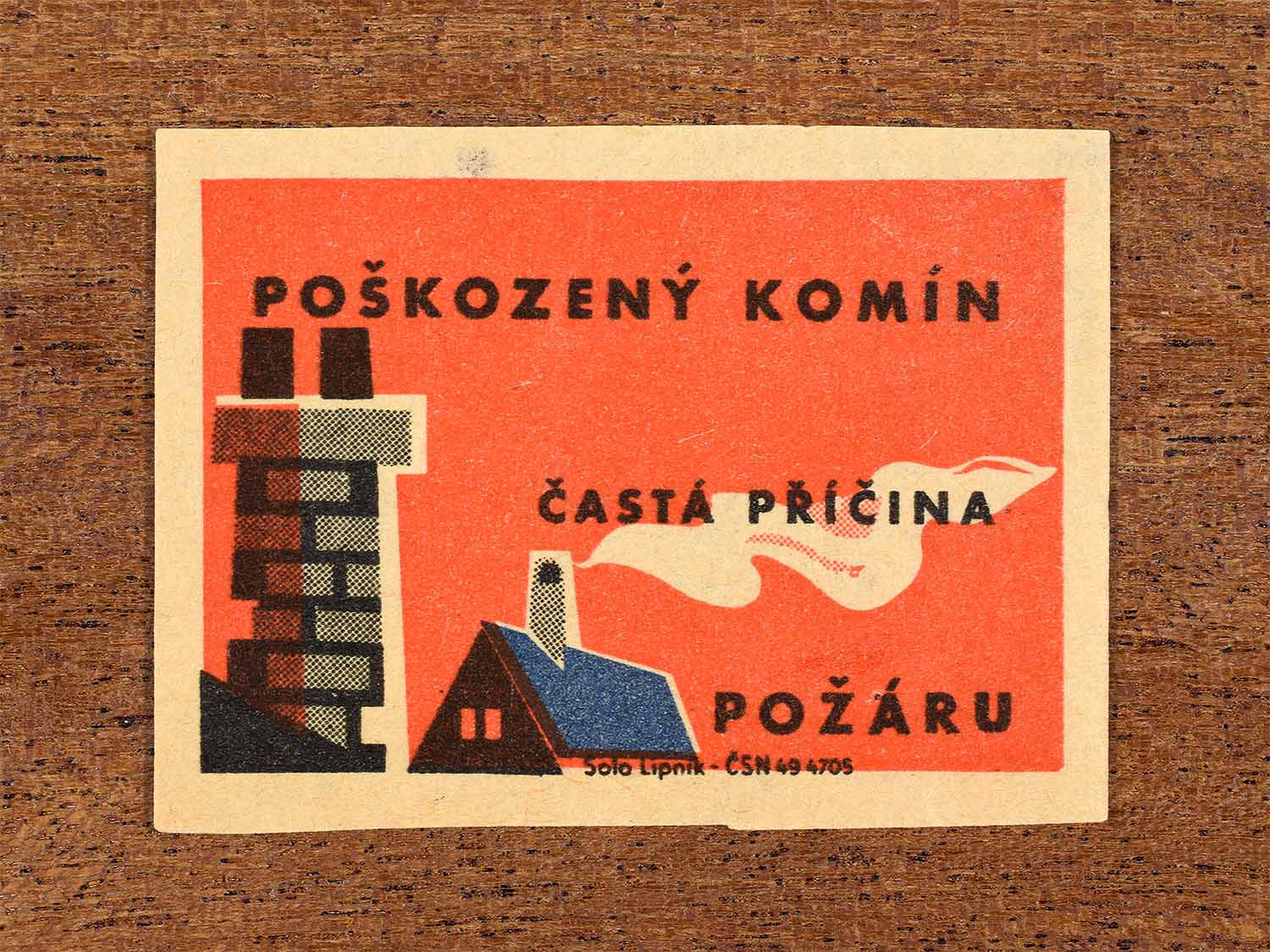 Vintage 1964 Czech matchbox label showing the roof of a house with a working chimney, and a broken chimney, on red background. Produced by the Solo Lipník match factory to warn that damaged chimneys are a common cause of fires.