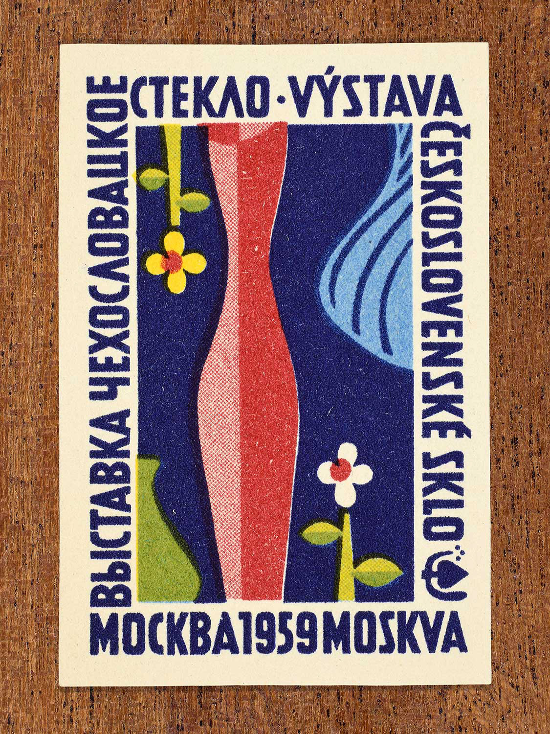 Vintage 1959 Czechoslovak matchbox label showing a tall red glass vessel surrounded by flowers against a dark blue background. Produced by an unknown factory to promote Czechoslovak artistic glass design at an international cultural event.