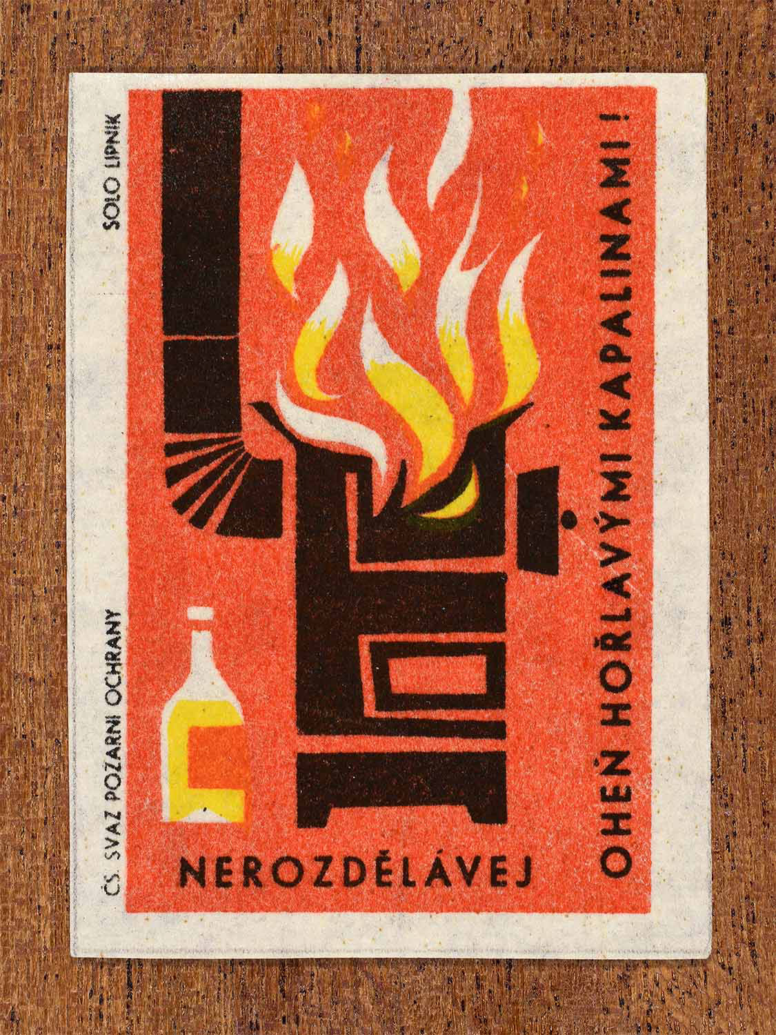 Vintage 1963 Czech matchbox label showing a stove and flames with a bottle of liquid in red, black and yellow colours. Produced by the Solo Lipník match factory to warn against using flammable liquids to start fires.