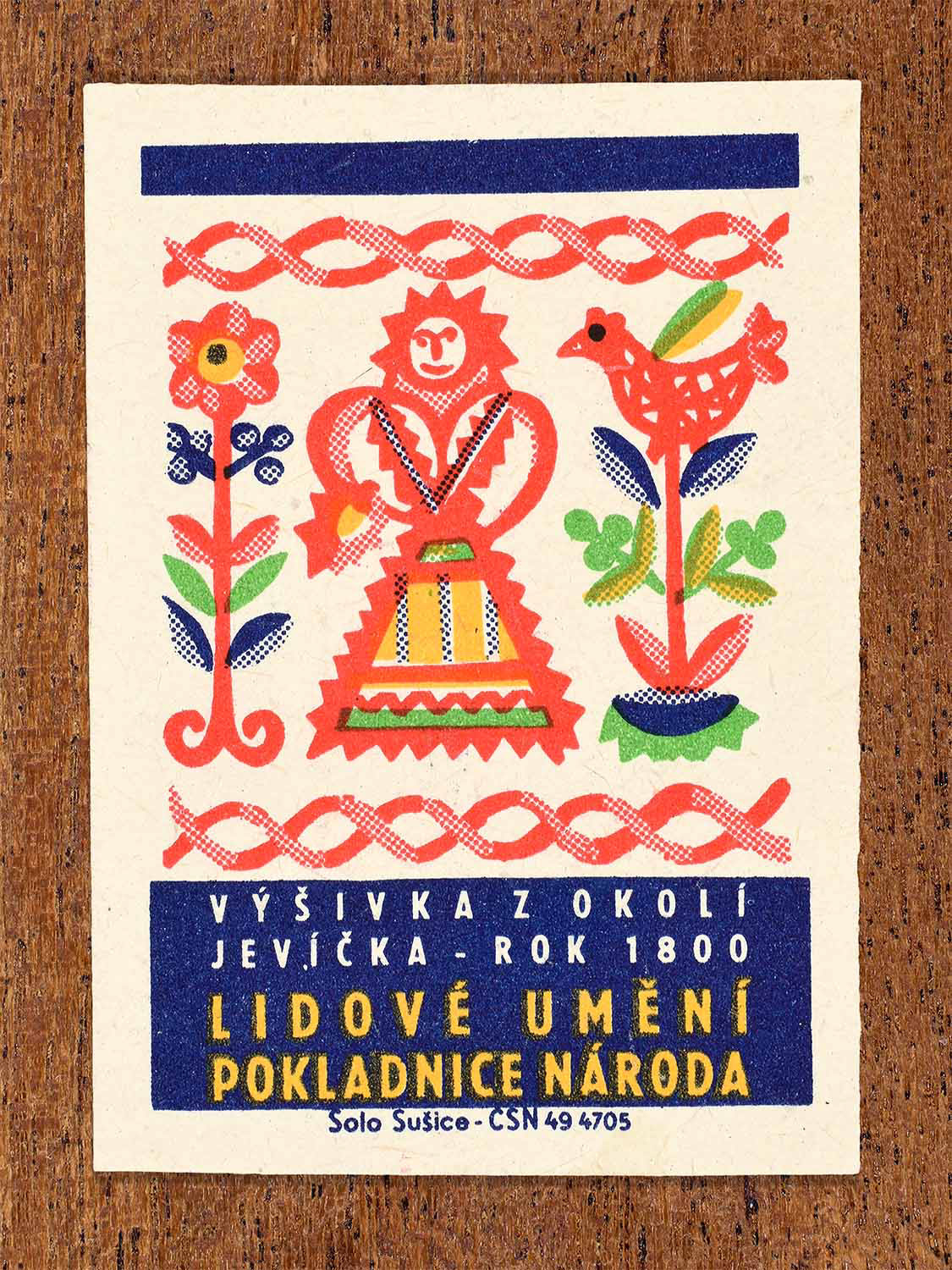Vintage 1964 Czech matchbox label showing a stylised female folk figure with floral embroidery motifs in red, blue and green. Produced by the Solo Sušice match factory to celebrate traditional embroidery from the Jevíčko region.