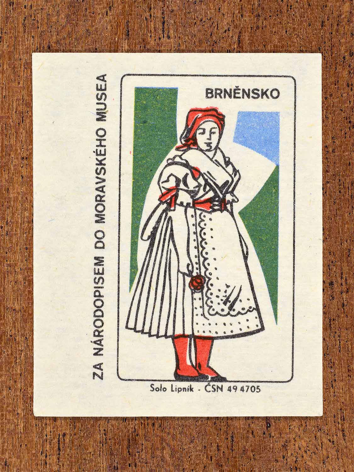 Vintage c. 1968 Czech matchbox label showing a female folk costume from the Brno region with white apron and red stockings. Produced by the Solo Lipník match factory to promote Moravian ethnography through the Moravian Museum.