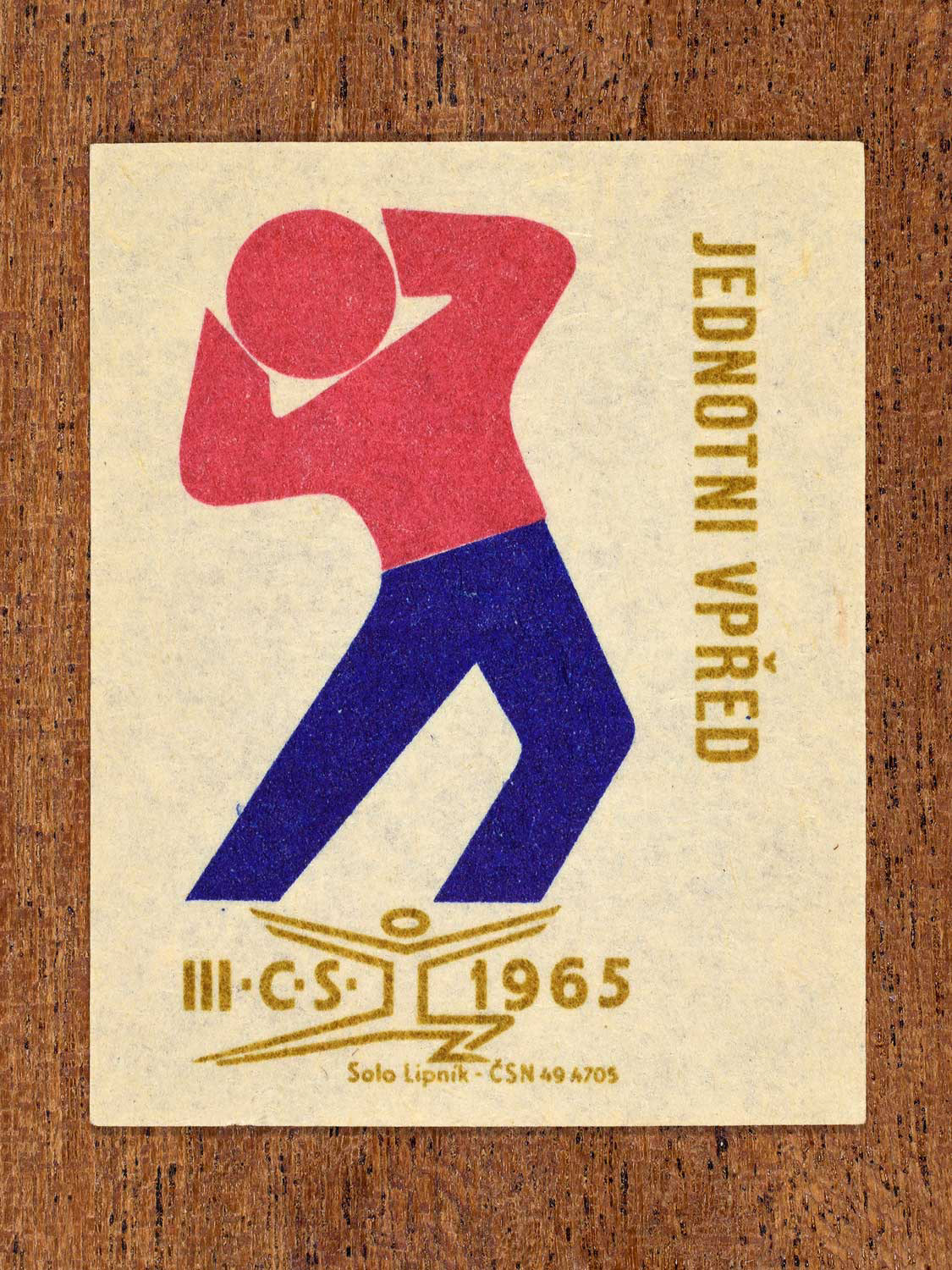 Vintage 1965 Czechoslovak matchbox label showing a stylised athlete in blue, red and gold colours. Produced by the Solo Lipník match factory to promote unity and collective progress.